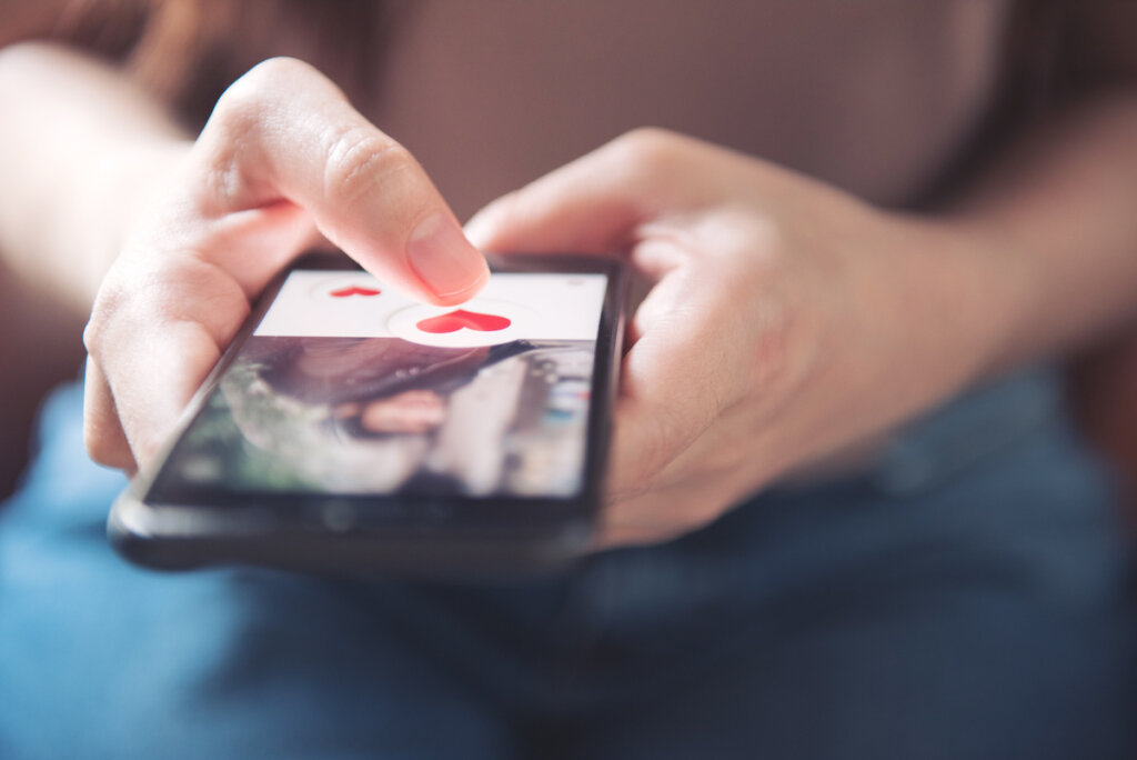 Close-up of a person's hand holding a smartphone, showing a dating app interface with a red heart symbol.