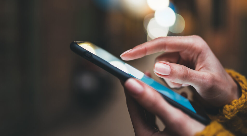 Close-up of a person's hand with manicured nails using a smartphone.